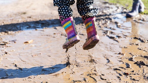 Child jumping in wellies above a muddy puddle.